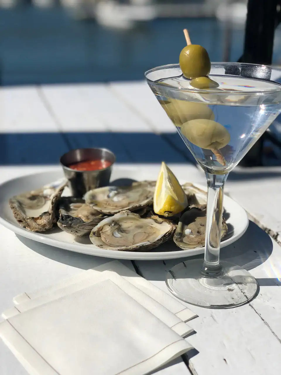 White folded organic cotton napkins on a table next to a martini and oysters at an outdoor dining setting