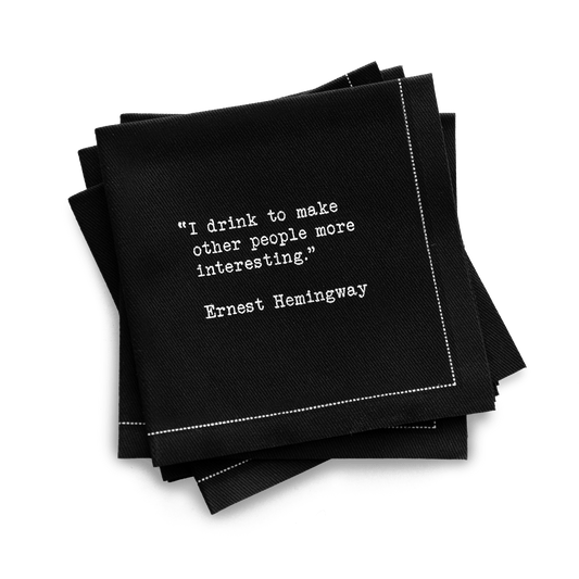 Quarter-fold organic cotton cocktail napkin, black, with white dotted border printed with the quote "I drink to make other people more interesting," from Five Star Napkins' Drinking Quotes First Edition collection