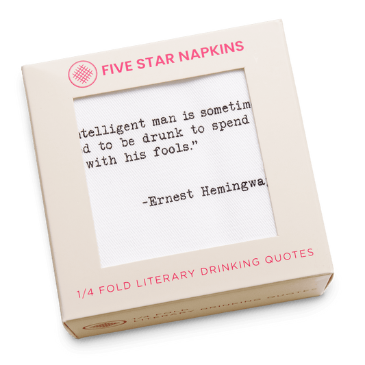 Kraft gift box from Five Star Napkins' Drinking Quotes Second Edition collection, showing an organic cotton quarter-fold napkin printed with the quote "An intelligent man is sometimes forced to be drunk to spend time with his fools"