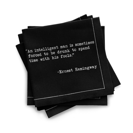 Organic cotton quarter-fold napkin, black, with white dotted border printed with the quote "An intelligent man is sometimes forced to be drunk to spend time with his fools," from Five Star Napkins' Drinking Quotes Second Edition collection