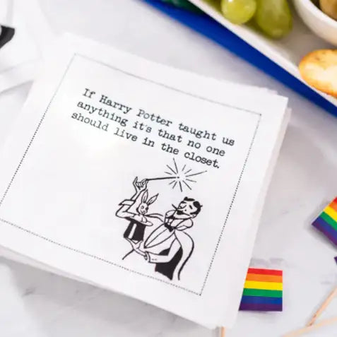 Organic cotton cocktail napkin with 'If Harry Potter taught us anything it's that no one should live in the closet' quote, styled on a table with rainbow flags and snacks.