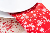 Red organic cotton napkin with white snowflake pattern under plate, festive table setting