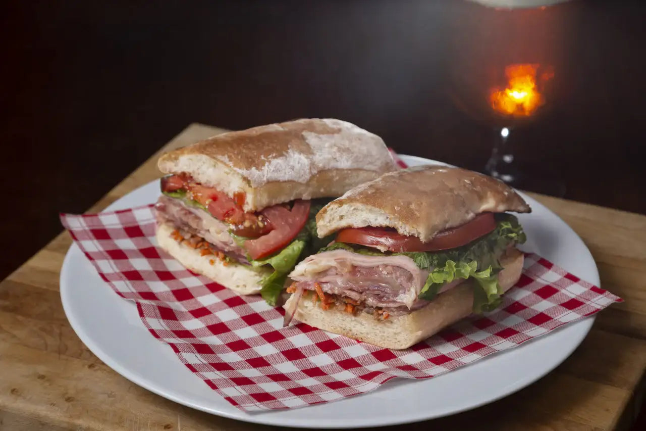 Two sandwich halves on a plate atop a red and white plaid organic cotton napkin