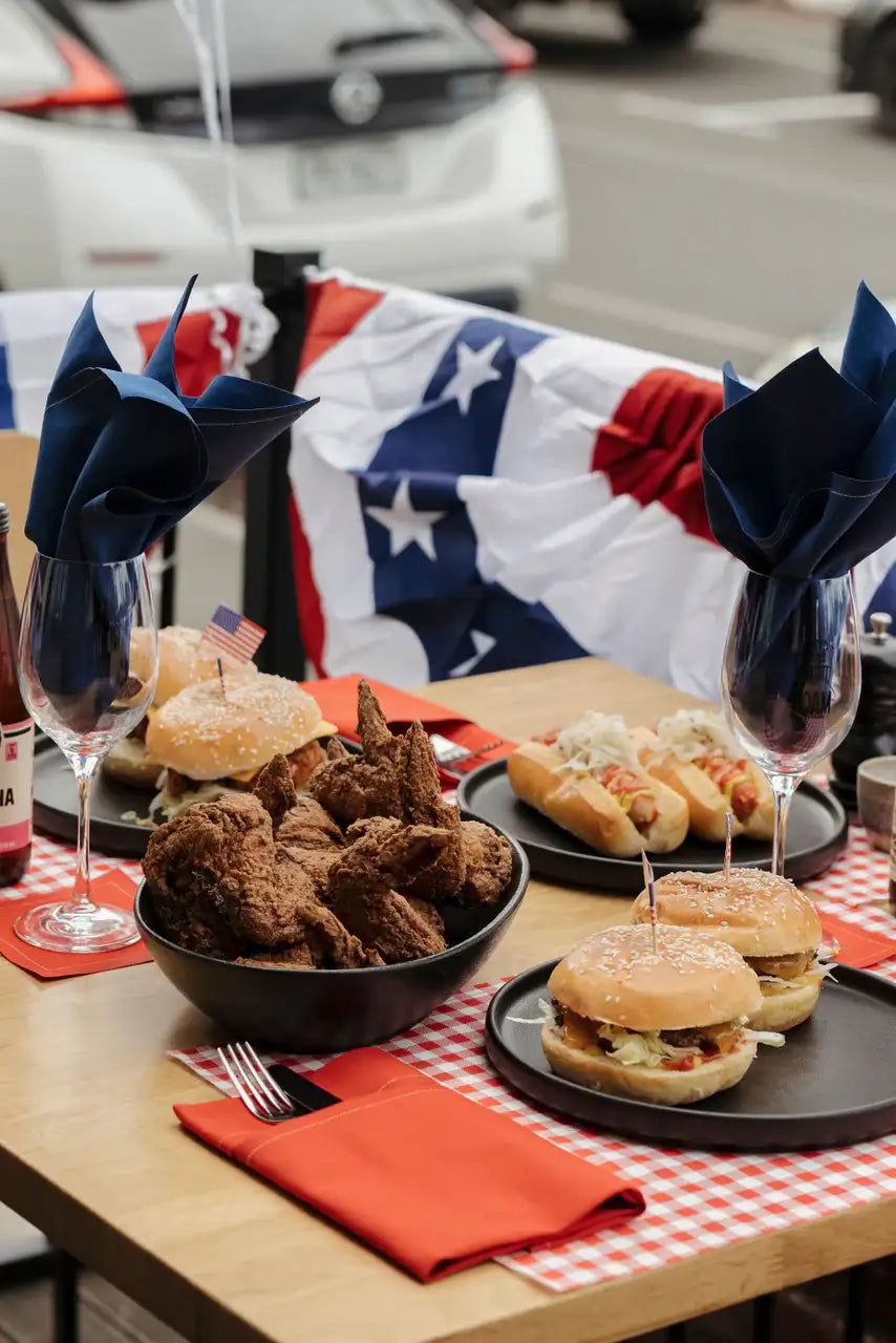 Outdoor table with burgers, fried chicken, hot dogs, and Persimmon organic cotton napkins in a picnic setting