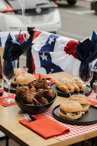 Outdoor table with burgers, fried chicken, hot dogs, and Persimmon organic cotton napkins in a picnic setting