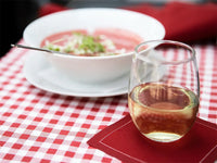 Glass of white wine on Persimmon organic cotton napkin beside bowl of soup on red check tablecloth
