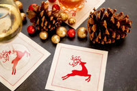 organic cotton cocktail napkins in Toreador with red reindeer print, styled with drinks, pinecones, and gold and red ornaments