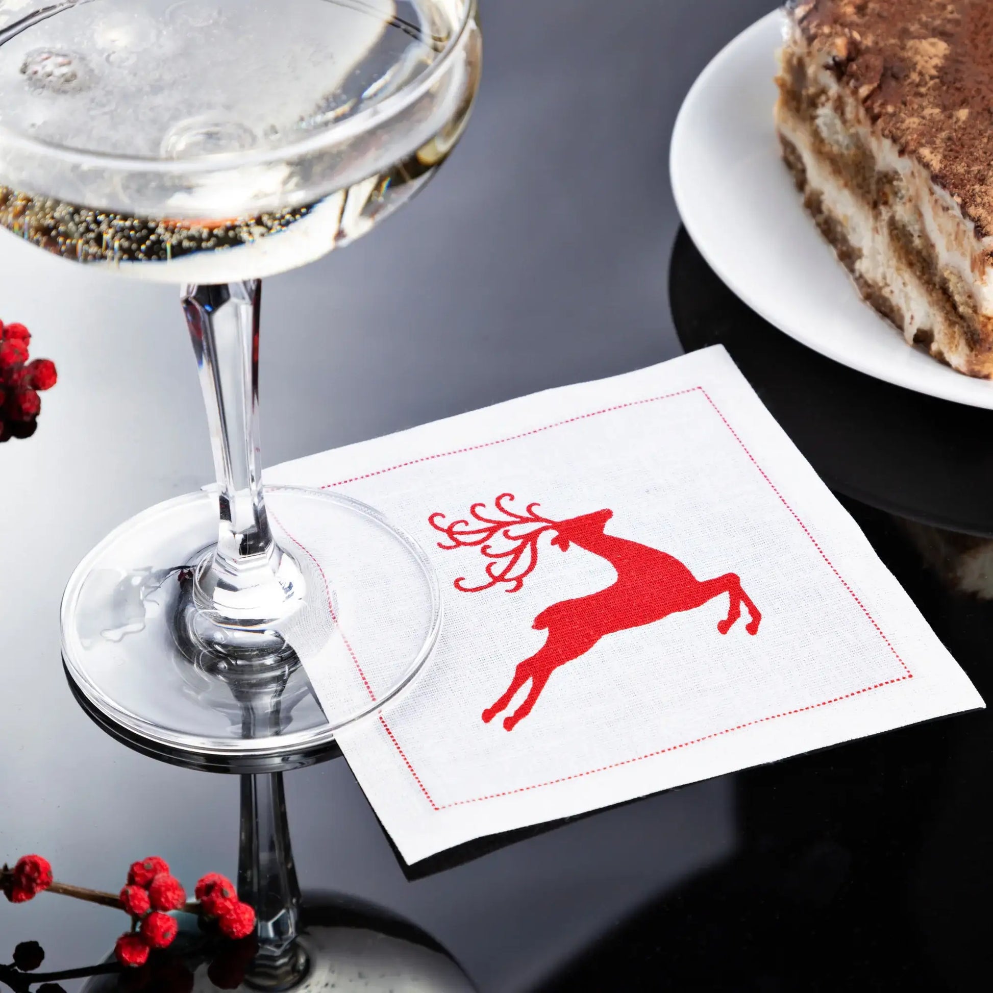 organic cotton cocktail napkin with Toreador red reindeer design, set on a table with dessert and drink