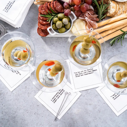 Organic cotton cocktail napkins with printed quotes next to martinis and charcuterie board at a party.