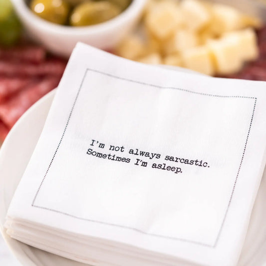 Organic cotton cocktail napkin printed with the quote "I'm not always sarcastic. Sometimes I'm asleep," styled on a plate with charcuterie and cheese, from Five Star Napkins' Snarky quote collection