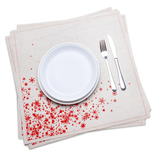 Natural organic cotton dinner napkins with a red snowflake print, dressed on a plate with silverware, by Five Star Napkins.