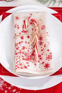 Organic cotton napkin with red snowflake pattern, folded on a white plate with a candy cane, holiday table setting