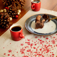 Organic cotton placemat with red snowflake pattern, cake plate, red mugs, pinecones