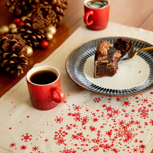 Organic cotton placemat with red snowflake pattern, cake plate, red mugs, pinecones