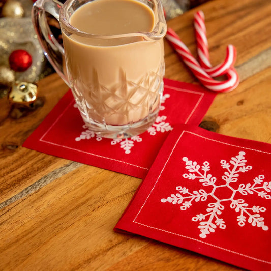 Toreador organic cotton cocktail napkins with white snowflake design on a wooden table, styled with a glass of creamy drink and candy canes.