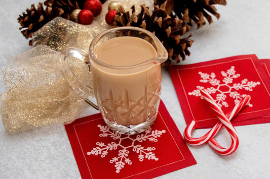 Holiday party setting with glass of eggnog, candy canes, pinecones, and red Persimmon organic cotton napkins featuring white snowflake design