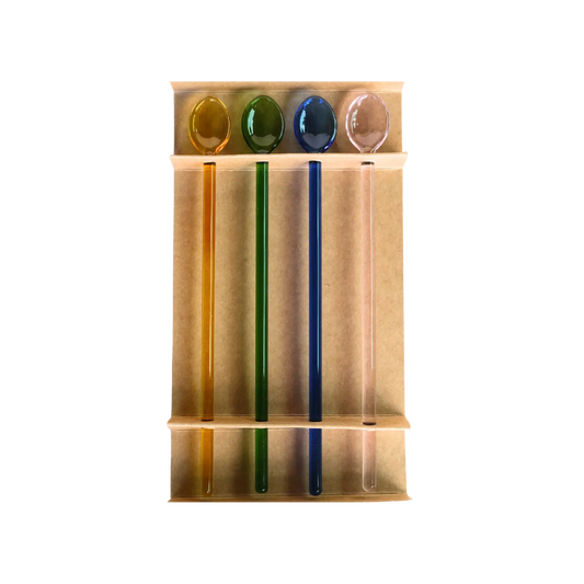 Four glass cocktail swizzle spoons in yellow, green, blue, and pink displayed in their kraft packaging tray.