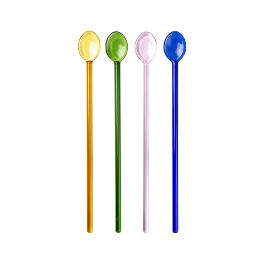 Four glass cocktail swizzle spoons in yellow, green, pink, and blue, standing upright against a white background.