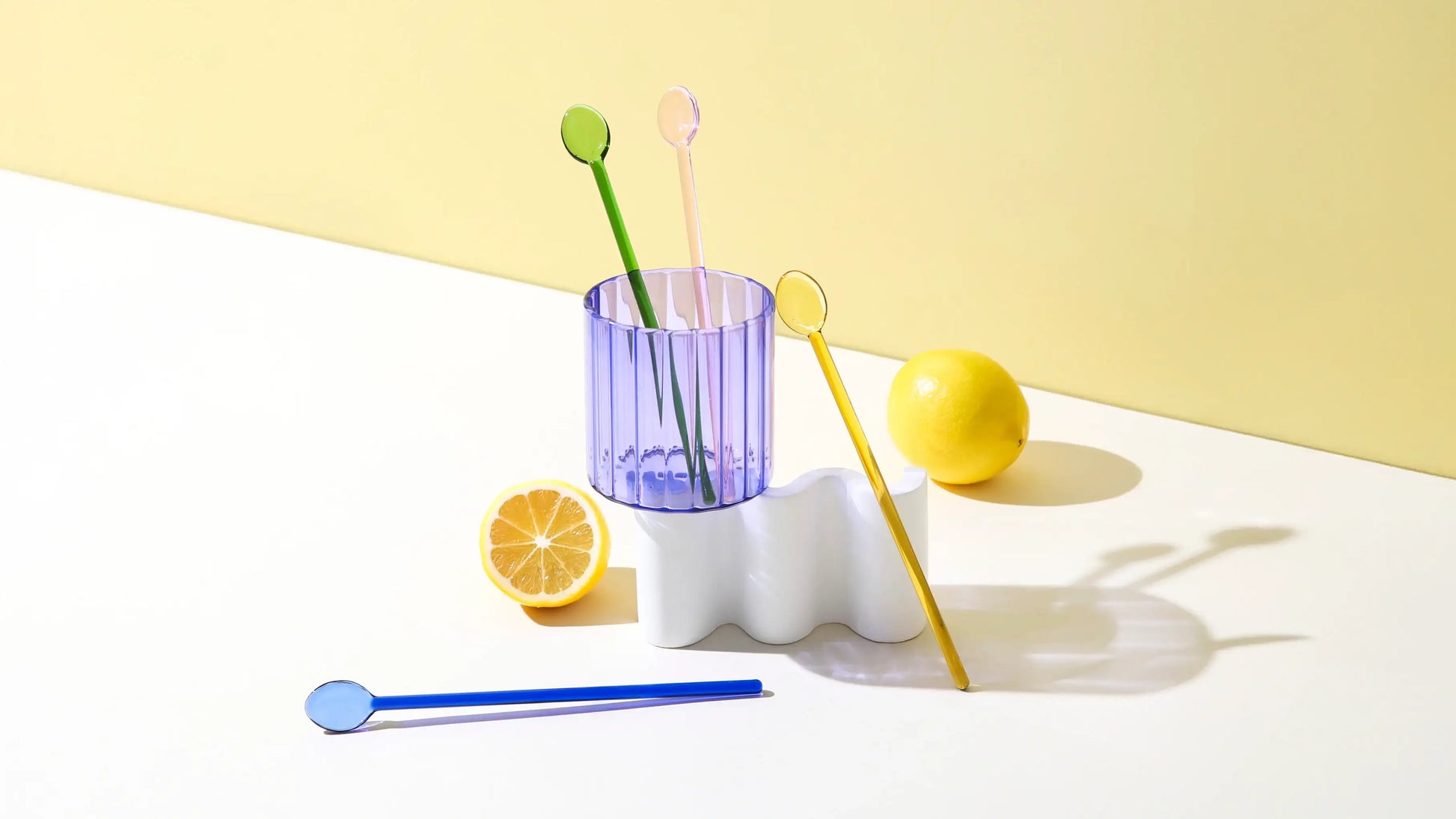 Glass cocktail swizzle spoons in a citrus-inspired lifestyle scene with fresh lemons and a ribbed glass, styled on a sunlit tabletop.