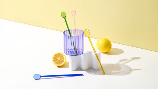 Glass cocktail swizzle spoons in a citrus-inspired lifestyle scene with fresh lemons and a ribbed glass, styled on a sunlit tabletop.