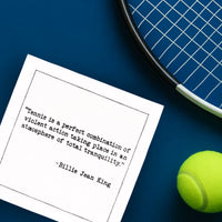 Organic cotton cocktail napkin printed with the quote “Tennis is a perfect combination of violent action taking place in an atmosphere of total tranquility,” – Billie Jean King, styled with a tennis racket and ball on a blue court, from Five Star Napkins’ Tennis Legends quote collection.