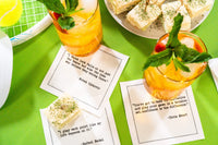 Organic cotton cocktail napkins printed with tennis quotes from Novak Djokovic, Chris Evert, and Rafael Nadal, styled with citrus cocktails and tea sandwiches on a tennis court, from Five Star Napkins’ Tennis Legends quote collection.