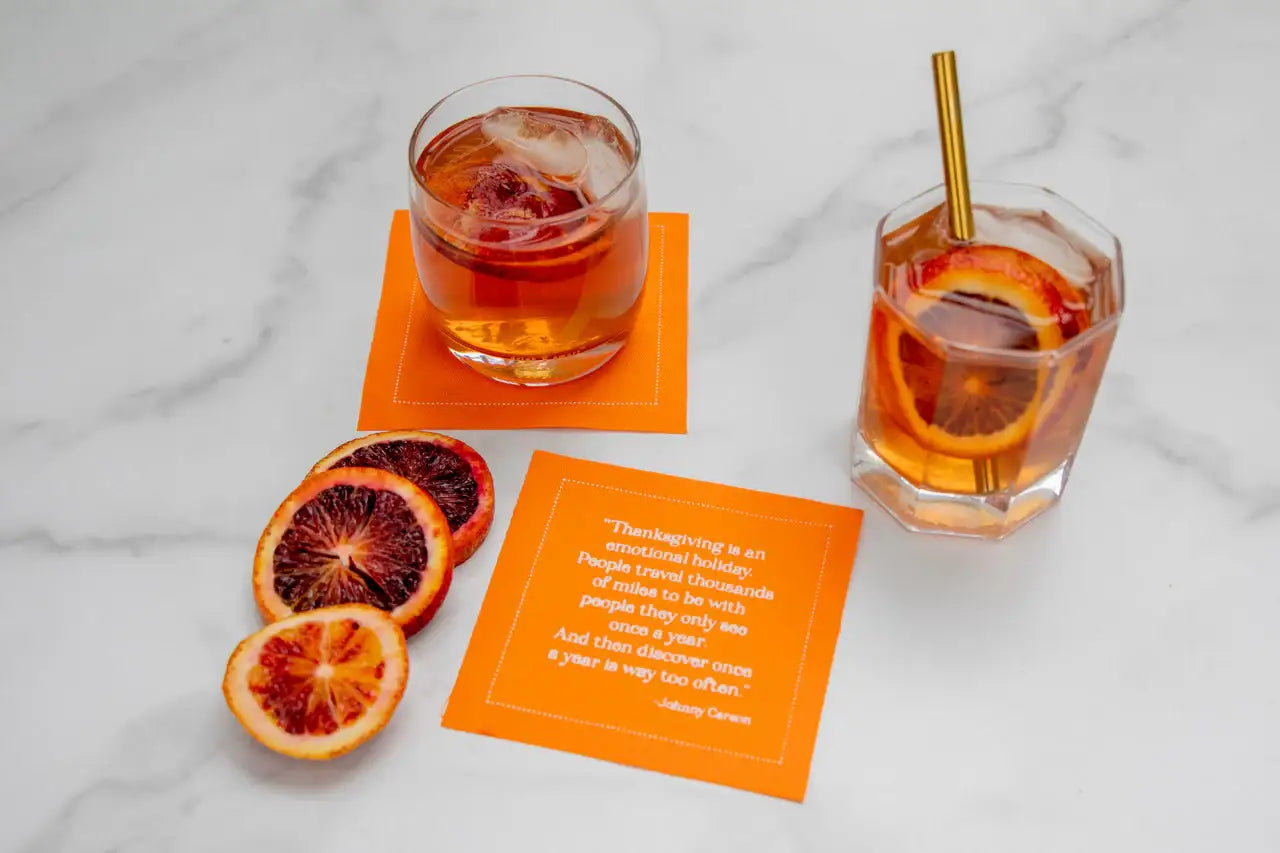Organic cotton Persimmon quote cocktail napkin with printed Thanksgiving quote, drinks, and citrus slices on marble surface