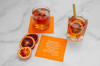 Organic cotton Persimmon quote cocktail napkin with printed Thanksgiving quote, drinks, and citrus slices on marble surface