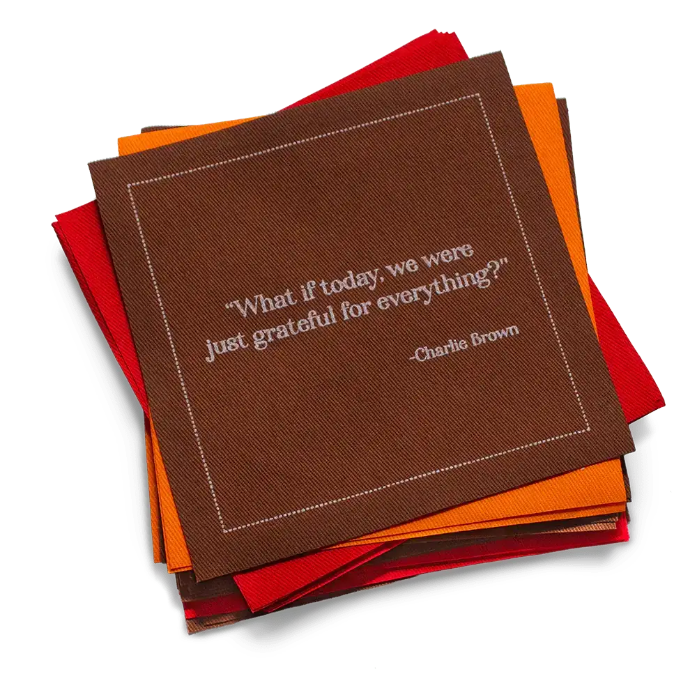 Stack of red, orange, and brown organic cotton cocktail napkins with the printed quote, “What if today, we were just grateful for everything?” – Charlie Brown.