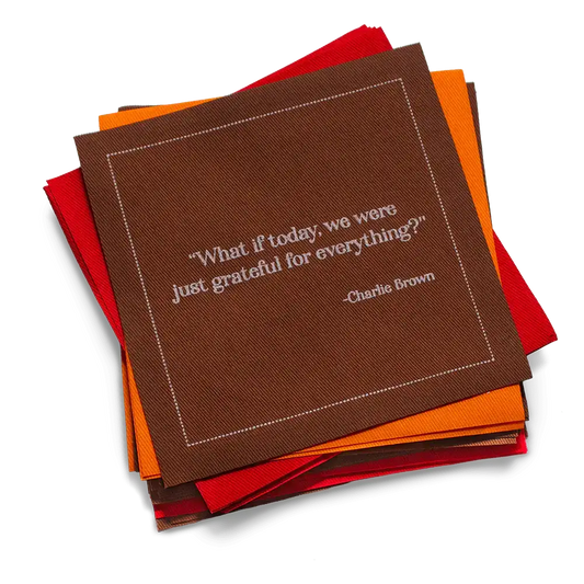 Stack of red, orange, and brown organic cotton cocktail napkins with the printed quote, “What if today, we were just grateful for everything?” – Charlie Brown.