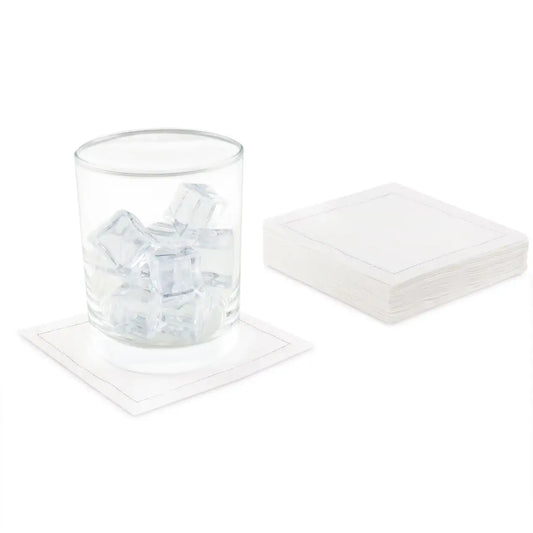 White Signature organic cotton cocktail napkins, one under a glass with ice, stacked pack beside