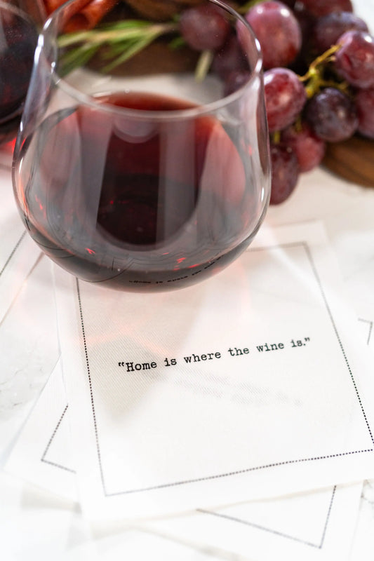 Organic cotton cocktail napkin printed with the quote "Home is where the wine is," styled under a wine glass with grapes, from Five Star Napkins' Wine quote collection
