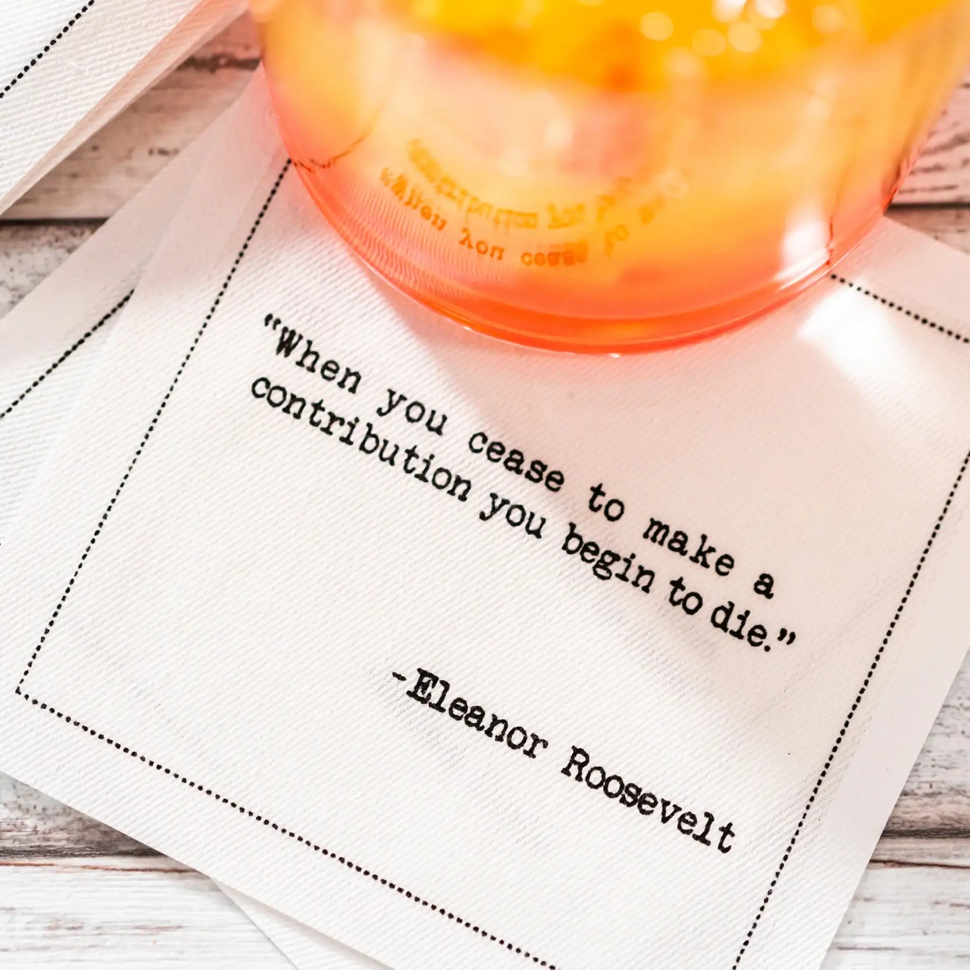 Organic cotton cocktail napkin with printed quote 'When you cease to make a contribution you begin to die.'